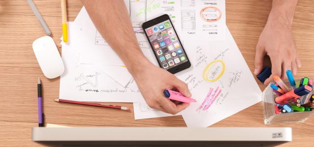 busy desk from above with man's hands taking notes